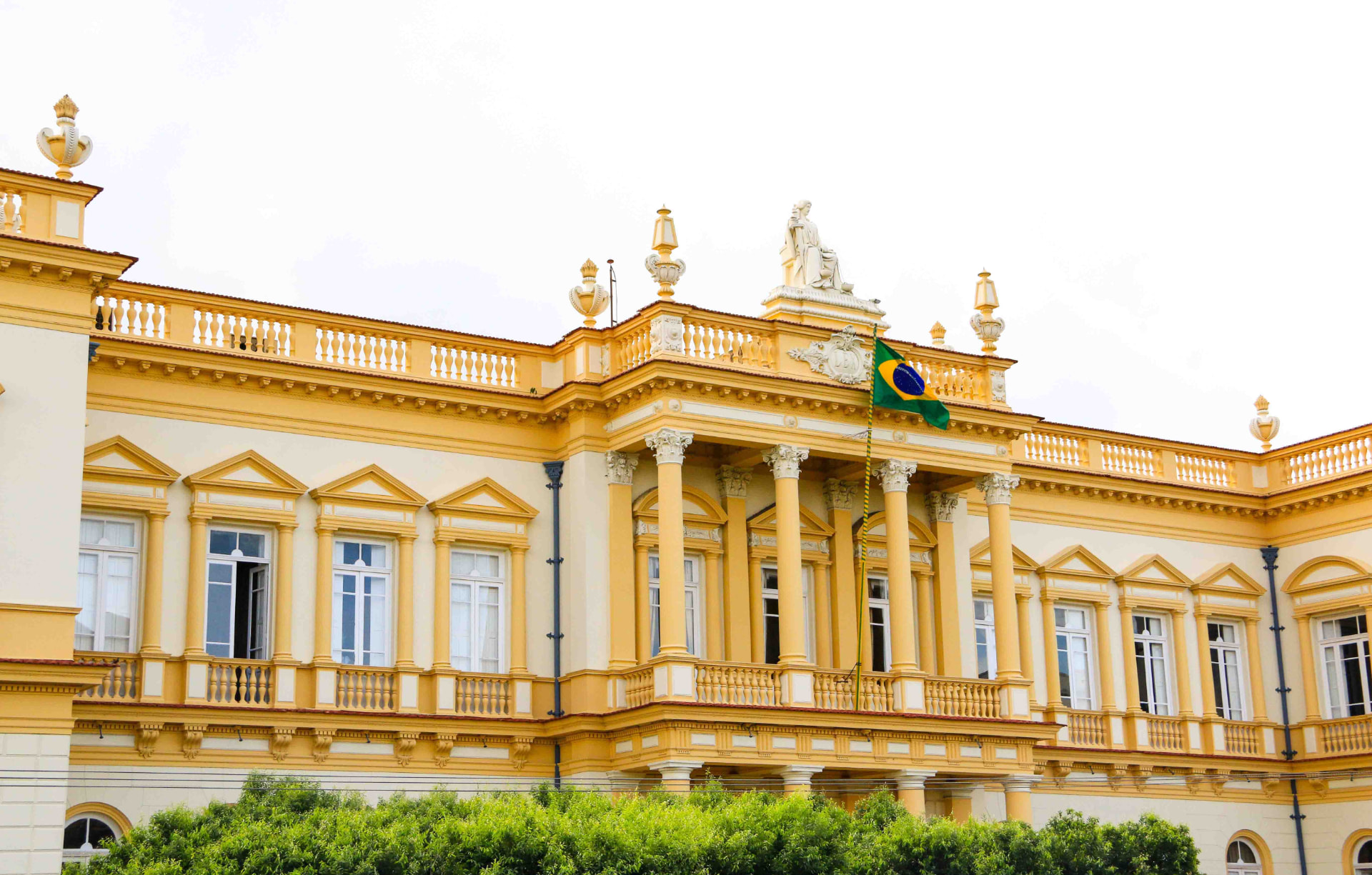 Fachada amarela e branca do Palácio da Justiça, com colunas e bandeira do Brasil