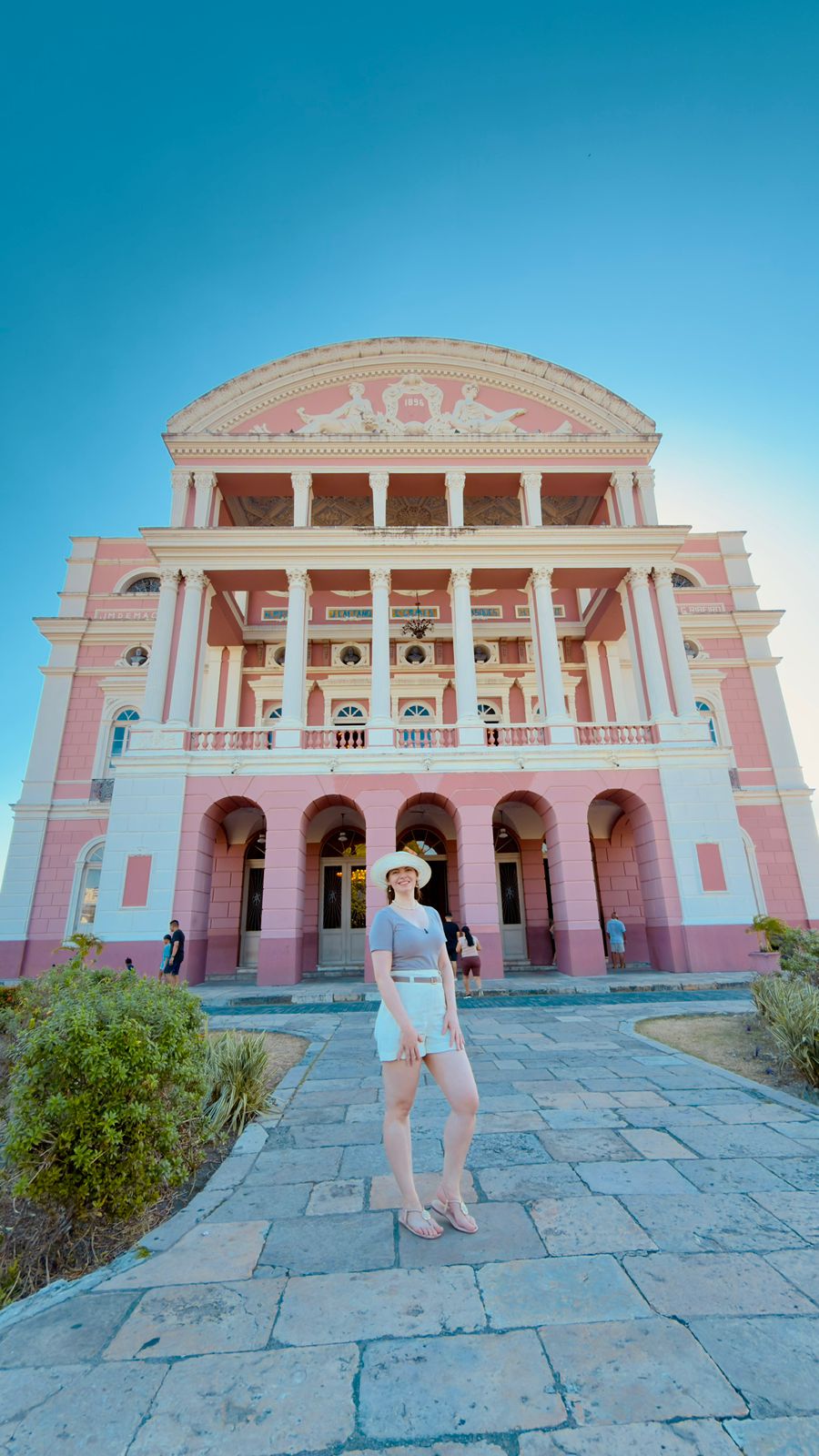 Fachada rosa do Teatro Amazonas vista de frente, com céu azul