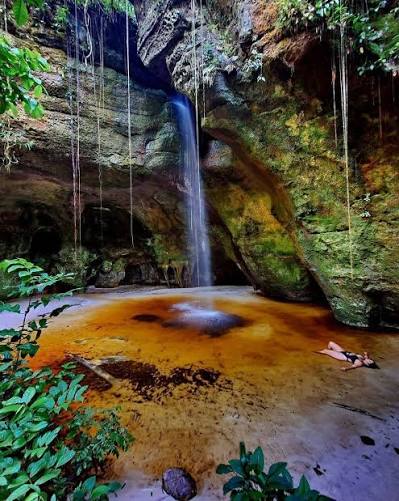Entrada estreita de gruta amazônica com feixe de luz e samambaias