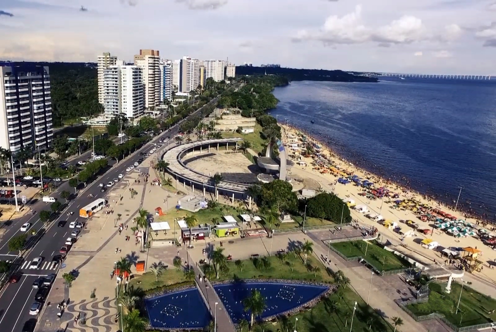 Orla com palmeiras e luzes da cidade refletindo na água ao anoitecer